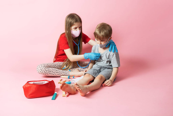 Persoonlijke beschermingsmiddelen: kinderen met medische maskers spelen dokter en een tienermeisje luistert naar de ademhaling van haar jongere broer. - Foto, afbeelding