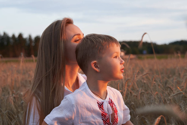 Portrait of cheerful son with camera sitting on mothers laps amidst wheat field. - Φωτογραφία, εικόνα