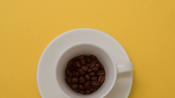 Stop motion animation of cup filling up with coffee beans on yellow - Felvétel, videó