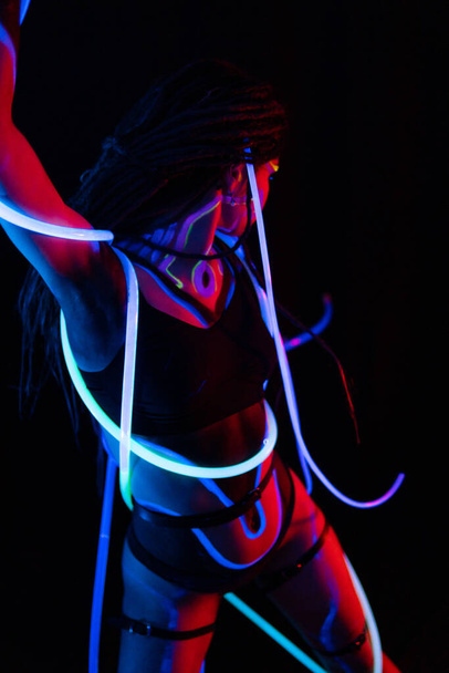 Portrait of a Warror Girl with Glowing Tubes in Neon UF Light. Model Girl with Dreadlocks and Fluorescent Creative Psychedelic MakeUp, Art Design of Female Disco Dancer Model in UV, Colorful Abstract - 写真・画像