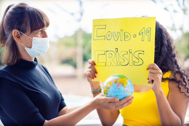 Tüm gezegendeki insanların Coronavirus salgını ve salgını nedeniyle karantinaya alındığının bir sembolü olarak pankart ve toprak küresiyle gösteri yapan kadınlar. Resim - Fotoğraf, Görsel