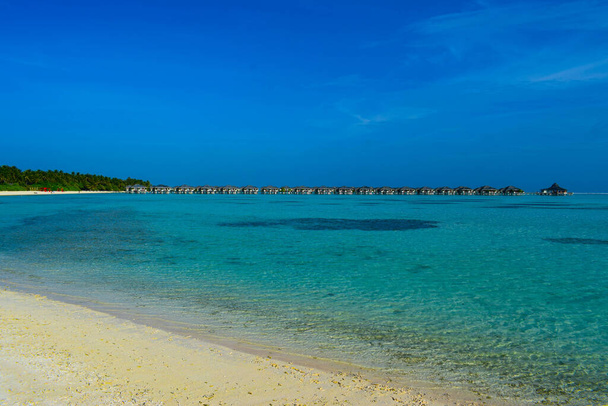 Ηλιόλουστη παραλία με λευκή άμμο, φοίνικες καρύδας και τυρκουάζ θάλασσα. Καλοκαιρινές διακοπές και τροπική παραλία έννοια. Πάνω από το νερό στο θέρετρο Maldive Island. - Φωτογραφία, εικόνα