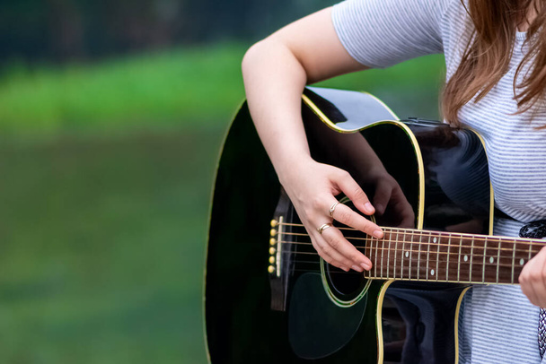Kaunis teini-ikäinen tyttö soittaa kitaraa istuessaan kivisillalla. Nuori nainen kitaristi ulkona luonnossa - Valokuva, kuva
