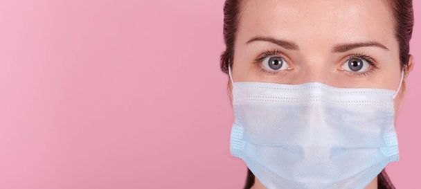 Portrait of a brunette girl in a medical mask. Isolated on pink background, banner. - Fotoğraf, Görsel
