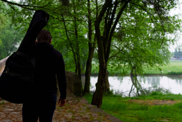 Jongeman draagt gitaartas terwijl hij alleen door het bos loopt. Genieten in de natuur schoonheid - Foto, afbeelding
