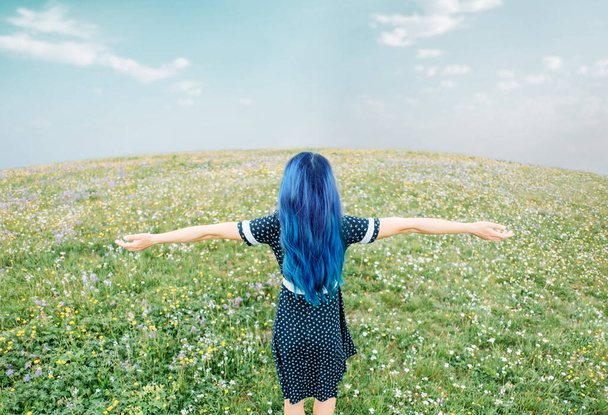 Blue hair young woman in dress resting with raised arms in summer meadow, rear view. - Photo, image