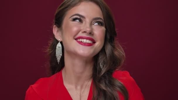 Μια κοντινή θέα μιας όμορφης ικανοποιημένης νεαρής γυναίκας που φοράει κόκκινο φόρεμα γελάει και ποζάρει απομονωμένη σε μπορντό φόντο - Πλάνα, βίντεο