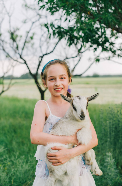 girl with baby goat on farm outdoors. Love and care. Village animals. happy child hugs goat, concept of unity of nature and man. Friendship of child and animals. Happy childhood. Girl and goat - Foto, Imagen