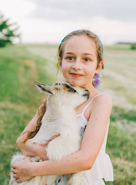 girl with baby goat on farm outdoors. Love and care. Village animals. happy child hugs goat, concept of unity of nature and man. Friendship of child and animals. Happy childhood. Girl and goat - Fotoğraf, Görsel