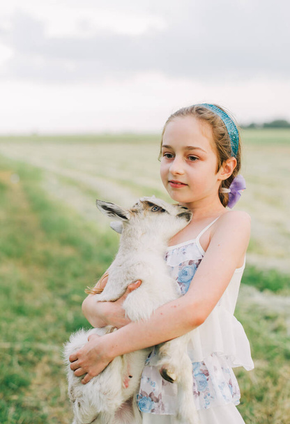 Çiftlikte keçi yavrusu olan bir kız. Sevgi ve ilgi. Köy hayvanları. Mutlu çocuk keçiye sarılır, doğanın ve insanın birliği kavramı. Çocuk ve hayvanların arkadaşlığı. Mutlu bir çocukluk. Kız ve keçi - Fotoğraf, Görsel