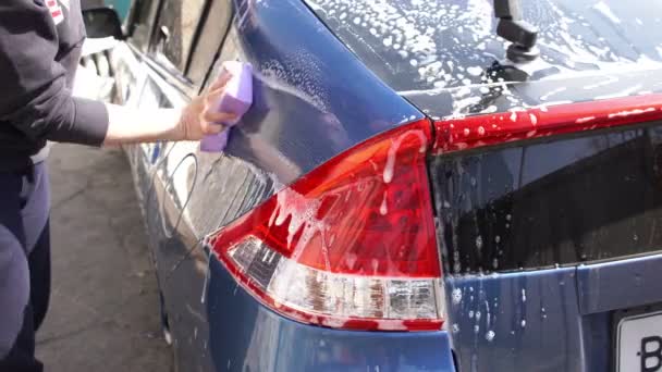 Henkilö pesee autoa saippualla ja sienellä kotona - Materiaali, video