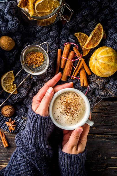 Φθινοπωρινό γλυκό ζεστό ρόφημα, Chai Buttered Rum, Pumpkin Pie ή Pumpkin Spice Coffee Latte. Άνετο φθινοπωρινό φόντο. Κορίτσι κατέχουν παραδοσιακό φλυτζάνι latte στα χέρια, σε ρουστίκ ξύλινο φόντο - Φωτογραφία, εικόνα