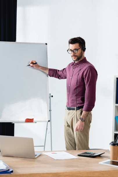 young businessman holding felt pen near flipchart while having video conference on laptop - Photo, Image