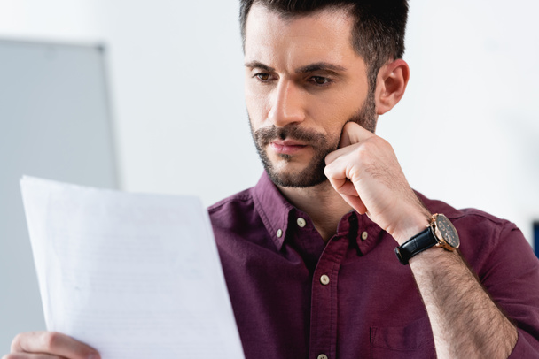 thoughtful, serious businessman touching chin while looking at document - Photo, image