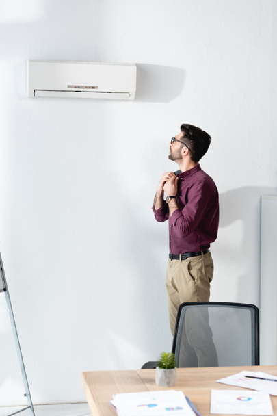 nuori liikemies, joka koskettaa paitaa seistessään ilmastointilaitteessa ja kärsii kuumuudesta  - Valokuva, kuva