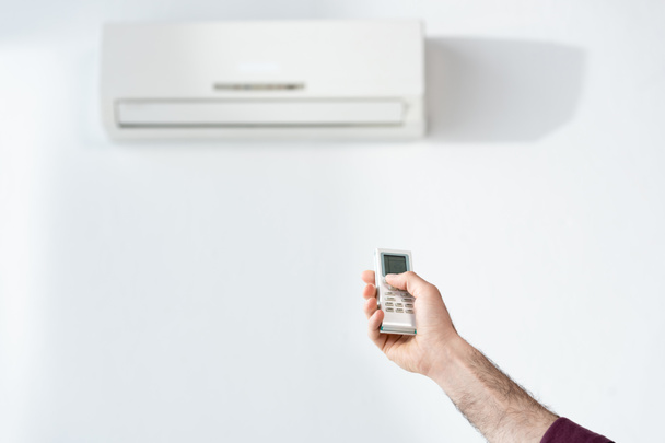 oříznutý pohled obchodníka zapínajícího klimatizaci v kanceláři s dálkovým ovladačem - Fotografie, Obrázek