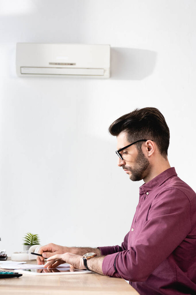 boční pohled pohledného podnikatele sedícího na pracovišti pod klimatizací - Fotografie, Obrázek