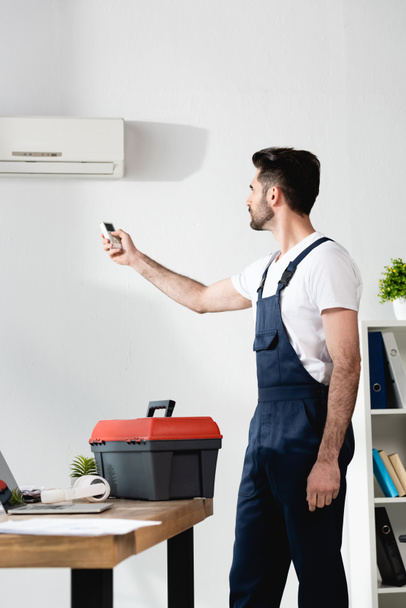 Korjaaja käyttää ilmastointilaite kaukosäädin seisoessaan lähellä työkalupakki - Valokuva, kuva