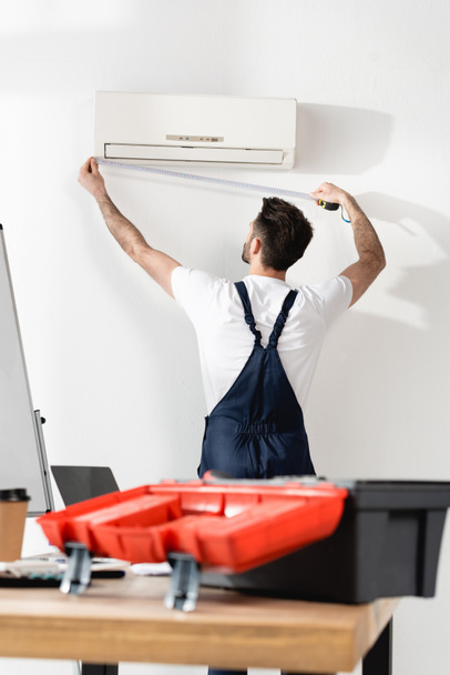 selectiive focus of repairman measuring air conditioner near office desk with toolbox - Photo, Image