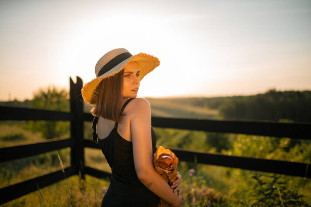Sunset photo of girl holding bread in her hands with hat in the field. - Photo, Image