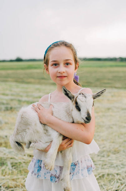 girl with baby goat on farm outdoors. Love and care. Village animals. happy child hugs goat, concept of unity of nature and man. Friendship of child and animals. Happy childhood. Girl and goat - Photo, image