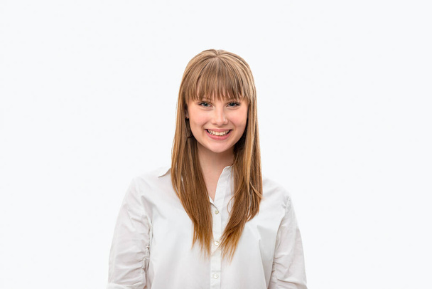 Waist up portrait of an attractive teenager girl with long hair and bangs wearing  white shirt against grey background - Foto, Imagen