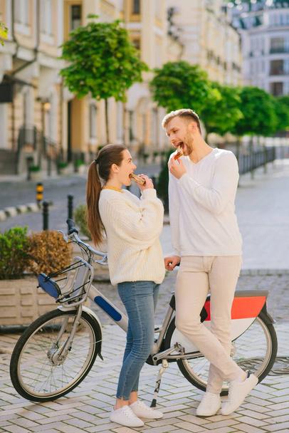 Man and woman standing near the bicycle eating sandwiches. - Fotografie, Obrázek