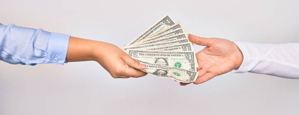 Dos manos de mujeres caucásicas haciendo transacciones. Mujer dando un montón de billetes de dólares a otra persona sobre fondo blanco aislado - Foto, imagen