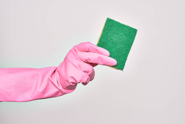 Hand of caucasian young woman wearing cleaning glove holding scourer sponge over isolated white background - Photo, Image