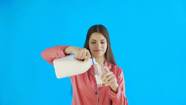 Привлекательная девушка в пижаме наливает молоко в стеклянную чашку
 - Фото, изображение