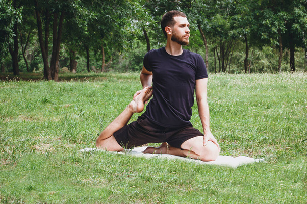 A young man practices yoga surrounded by a green tropical garden while relaxing in nature, stretching, meditation, Wellness. Striking techniques such as Muay Thai, karate outdoors - Foto, Bild