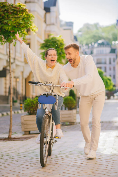 Energetic woman on bicycle and man nearby on the sidewalk - Photo, Image