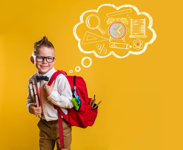 Happy schoolboy with backpack and books isolated on yellow background. - Фото, зображення