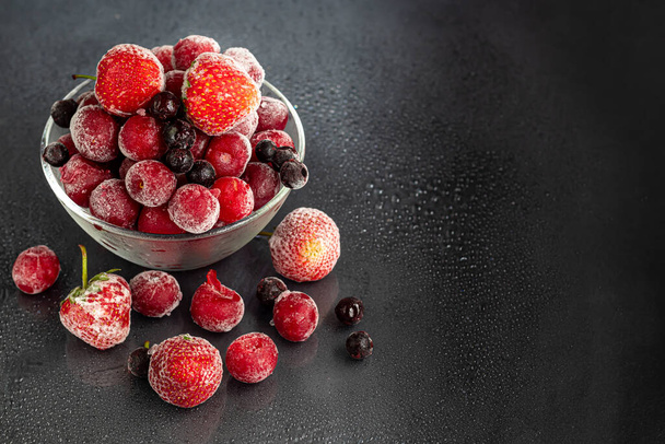 Gefrorene Früchte. Gefrorene Fruchtmischung aus Johannisbeeren, Kirschen und Erdbeeren. Vitaminmischung. Auf einem dunklen Hintergrund. Kopierraum. - Foto, Bild