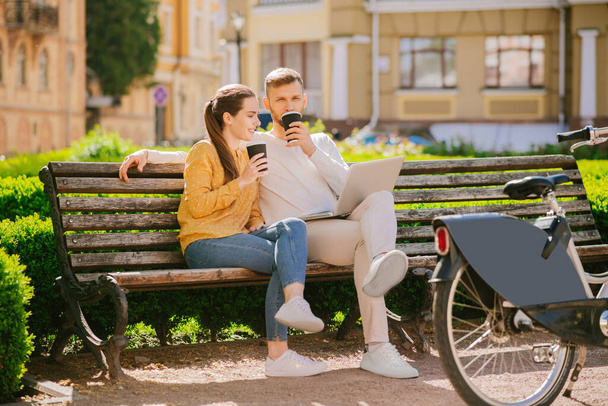 Man with laptop and woman sitting on a bench drinking coffee - Foto, immagini