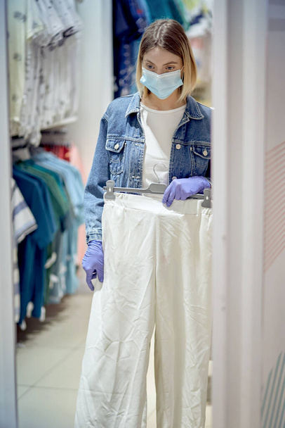 The girl near the mirror chooses pants in the mall. Girl in medical gloves. - Foto, immagini