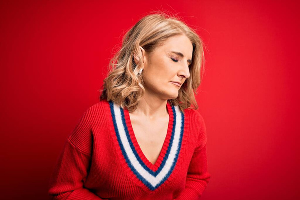 消化不良、痛みを伴う病気が体調不良のため、中年の美しいブロンドの女性は胃の上に手で孤立した赤い背景にカジュアルなセーターを着ています。アチェの概念. - 写真・画像