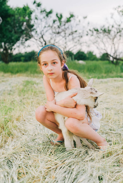 girl with baby goat on farm outdoors. Love and care. Village animals. happy child hugs goat, concept of unity of nature and man. Friendship of child and animals. Happy childhood. Girl and goat - Photo, Image