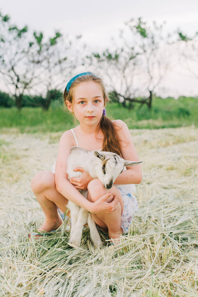 Dziewczyna z kozłem na farmie. Miłość i troska. Wiejskie zwierzęta. szczęśliwe dziecko przytula kozę, koncepcję jedności natury i człowieka. Przyjaźń dzieci i zwierząt. Szczęśliwego dzieciństwa. Dziewczyna i koza - Zdjęcie, obraz