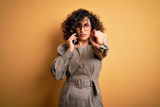Güzel Arap iş kadını gözlüklü, akıllı telefondan konuşuyor kamerayı işaret ediyor ve sen, el işareti, ön taraftan pozitif ve kendinden emin bir hareket. - Fotoğraf, Görsel