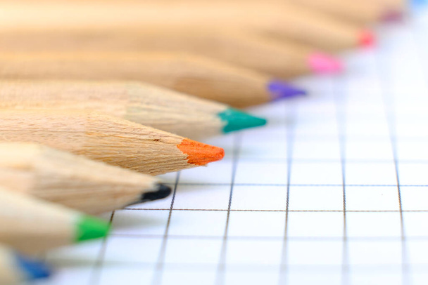 Closeup set van veelkleurige potloden op het geruite vel papier van notebook voor de tekening. Terug naar school concept. Kopieer ruimte, geen mensen. Ondiepe scherptediepte - Foto, afbeelding