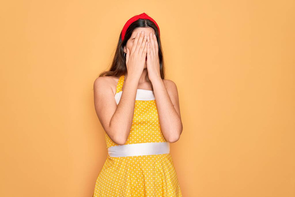 Młoda piękna pin się kobieta w 50s moda vintage sukienka na żółtym tle ze smutnym wyrazem twarzy z rąk podczas płaczu. Koncepcja depresji. - Zdjęcie, obraz