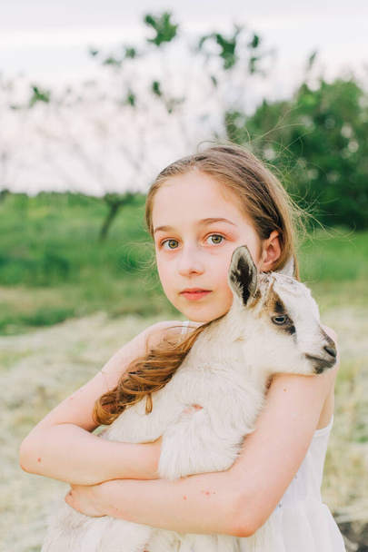 girl with baby goat on farm outdoors. Love and care. Village animals. happy child hugs goat, concept of unity of nature and man. Friendship of child and animals. Happy childhood. Girl and goat - Foto, Bild