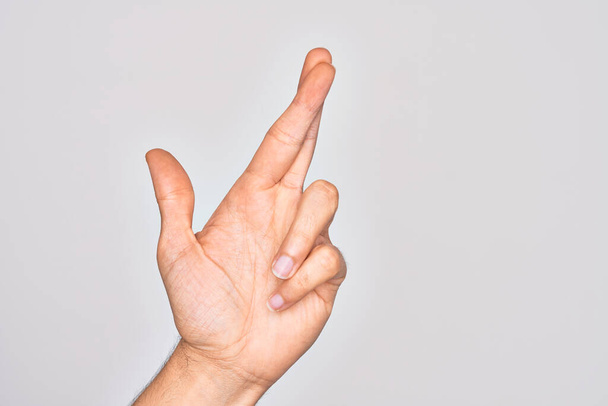 Hand of caucasian young man showing fingers over isolated white background gesturing fingers crossed, superstition and lucky gesture, lucky and hope expression - Photo, Image