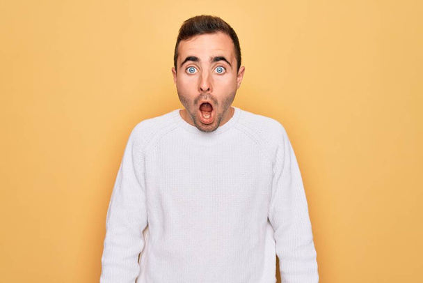 Young handsome man with blue eyes wearing casual sweater standing over yellow background afraid and shocked with surprise and amazed expression, fear and excited face. - Photo, Image