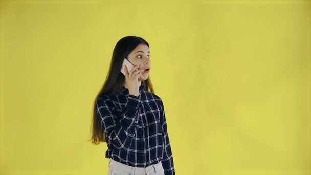 Überraschte Frau steht isoliert vor gelbem Hintergrund, während sie telefoniert - Foto, Bild