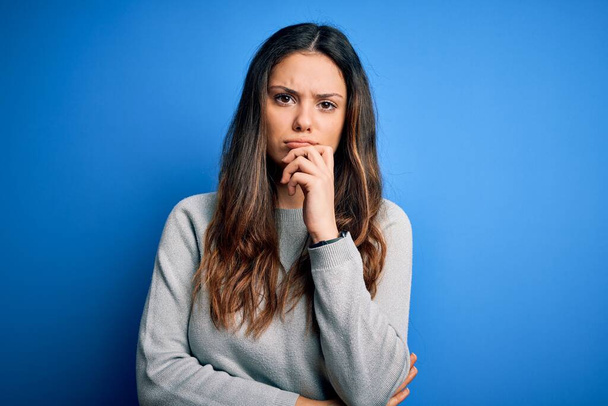 Young beautiful brunette woman wearing casual sweater standing over blue background with hand on chin thinking about question, pensive expression. Smiling with thoughtful face. Doubt concept. - Photo, Image
