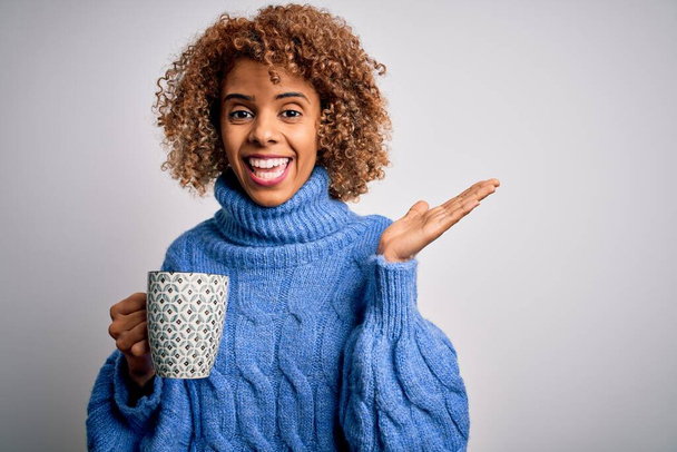 Young african american curly woman drinking mug of coffee over isolated white background very happy and excited, winner expression celebrating victory screaming with big smile and raised hands - Photo, image