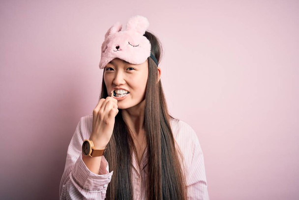 Jovem bela mulher asiática vestindo pijama escovar os dentes usando escova de dentes e pasta oral, limpeza de dentes e língua como rotina de manhã de cuidados de saúde saudável
 - Foto, Imagem