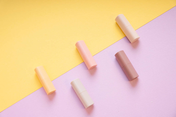 Kommerzielles Produkt - Gruppe pastellbeiger Lippenstifte auf gelbem und lila Hintergrund. - Foto, Bild